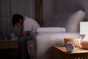 Man sitting in a dark bedroom at night with his head in his hands, unable to sleep